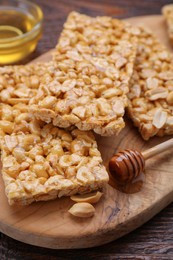 Delicious peanut bars (kozinaki) and dipper with honey on wooden table, closeup