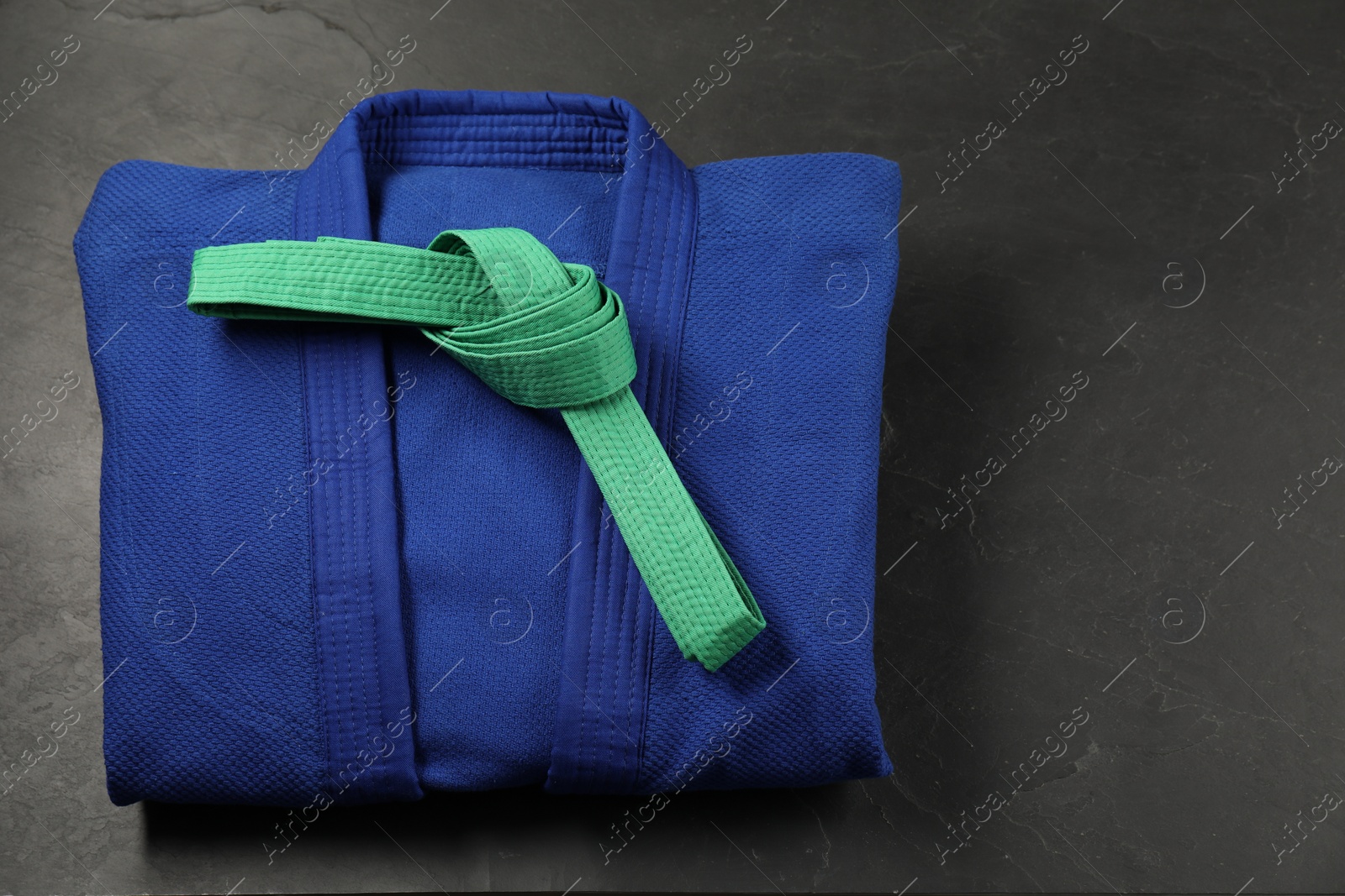 Photo of Green karate belt and blue kimono on gray background, top view. Space for text