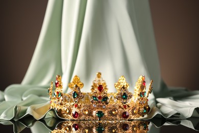 Beautiful golden crown with gems near light cloth on black table