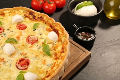 Photo of Delicious homemade cheese quiche and ingredients on black table, closeup