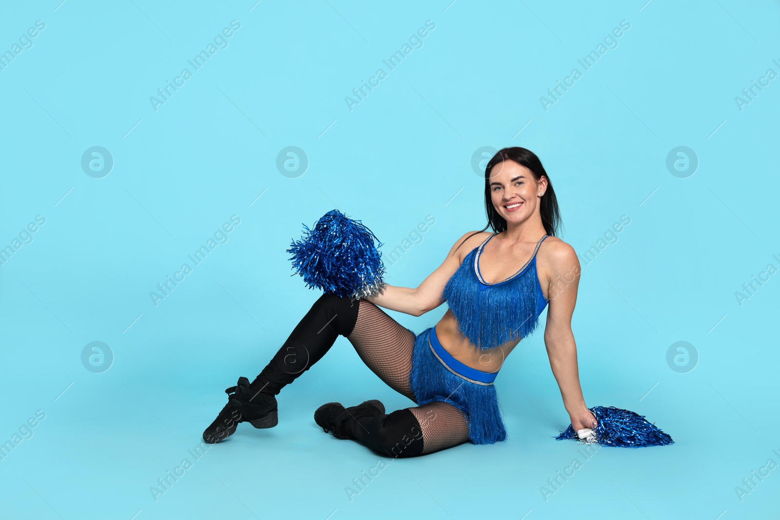 Photo of Beautiful cheerleader in costume holding pom poms on light blue background