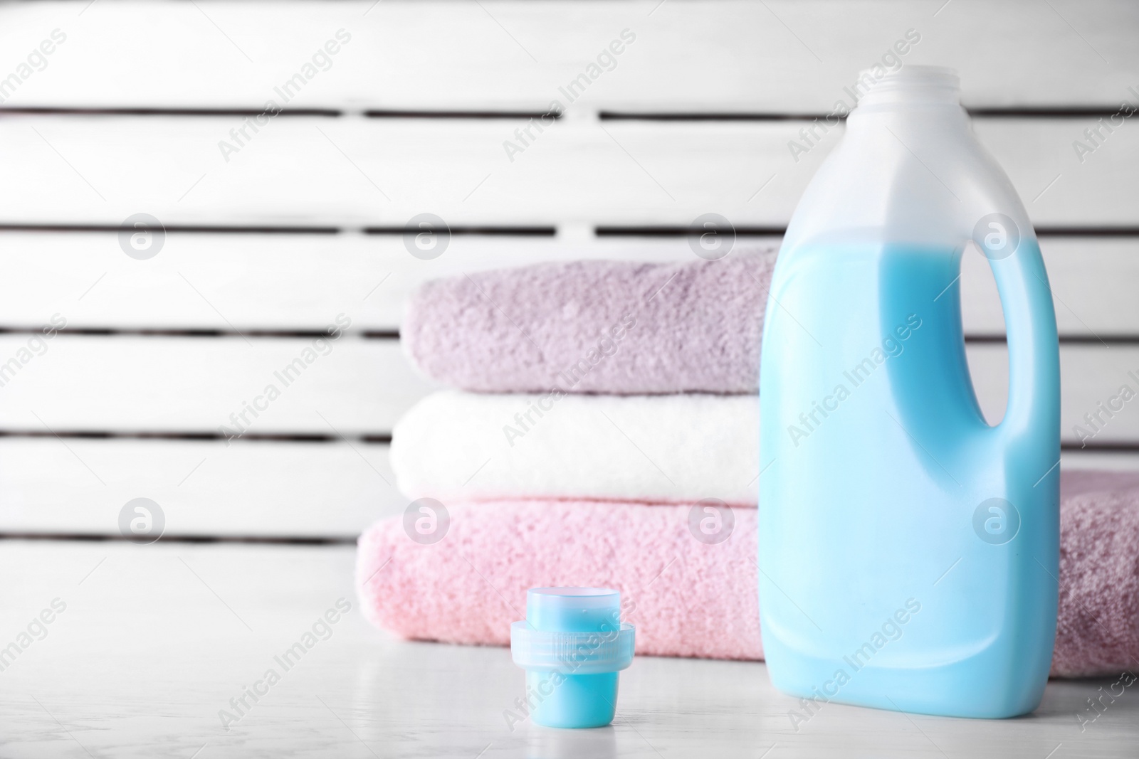 Photo of Laundry detergent and clean towels on table against blurred background. Space for text