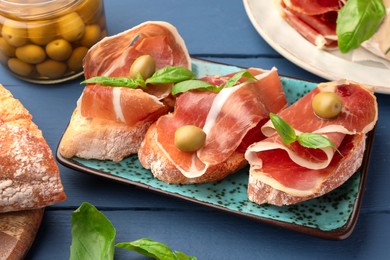 Photo of Tasty sandwiches with cured ham and basil leaves on blue wooden table