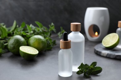 Photo of Bottles of essential oil, sliced limes and mint on grey table, space for text