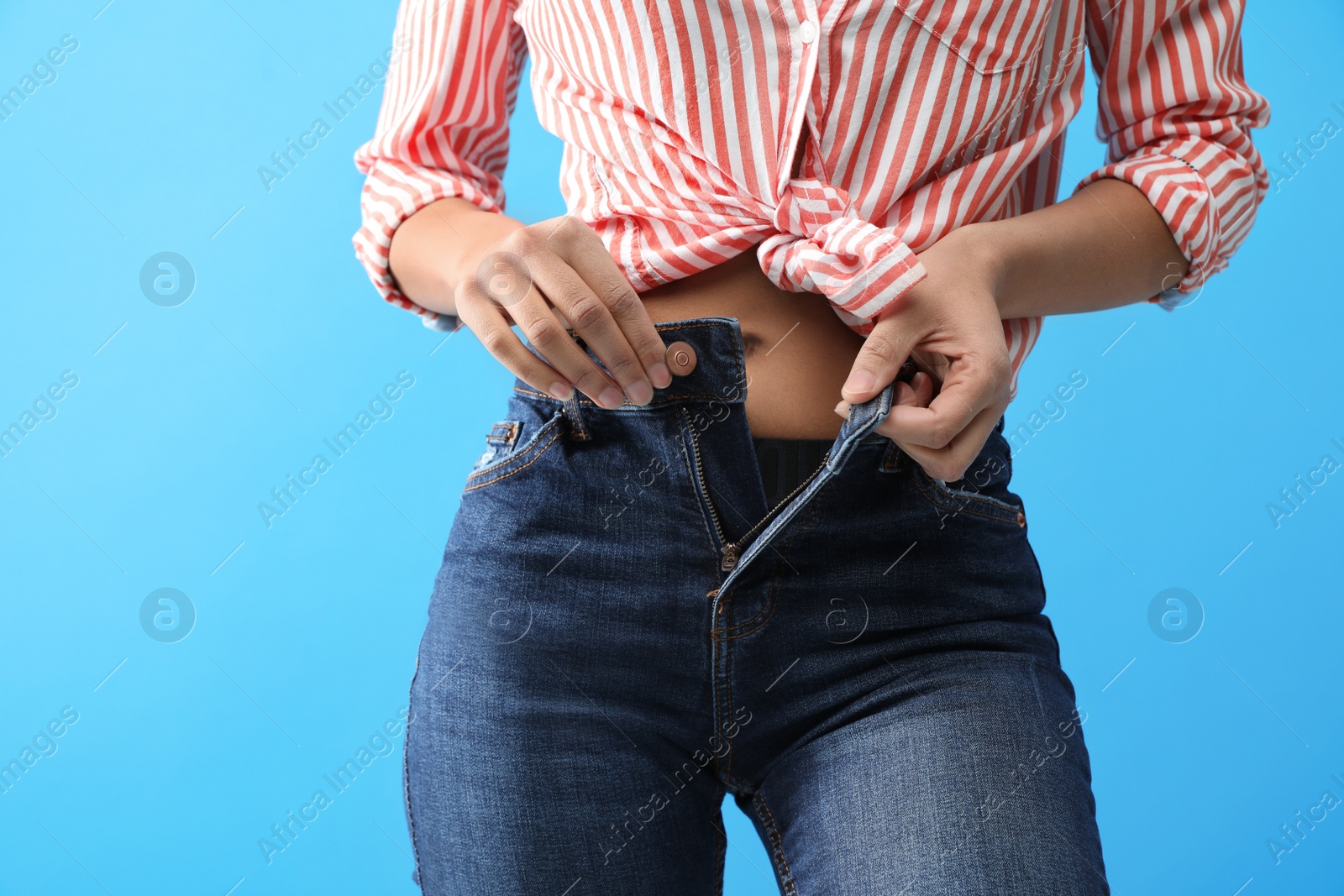 Photo of Woman unbuttoning jeans on blue background, closeup