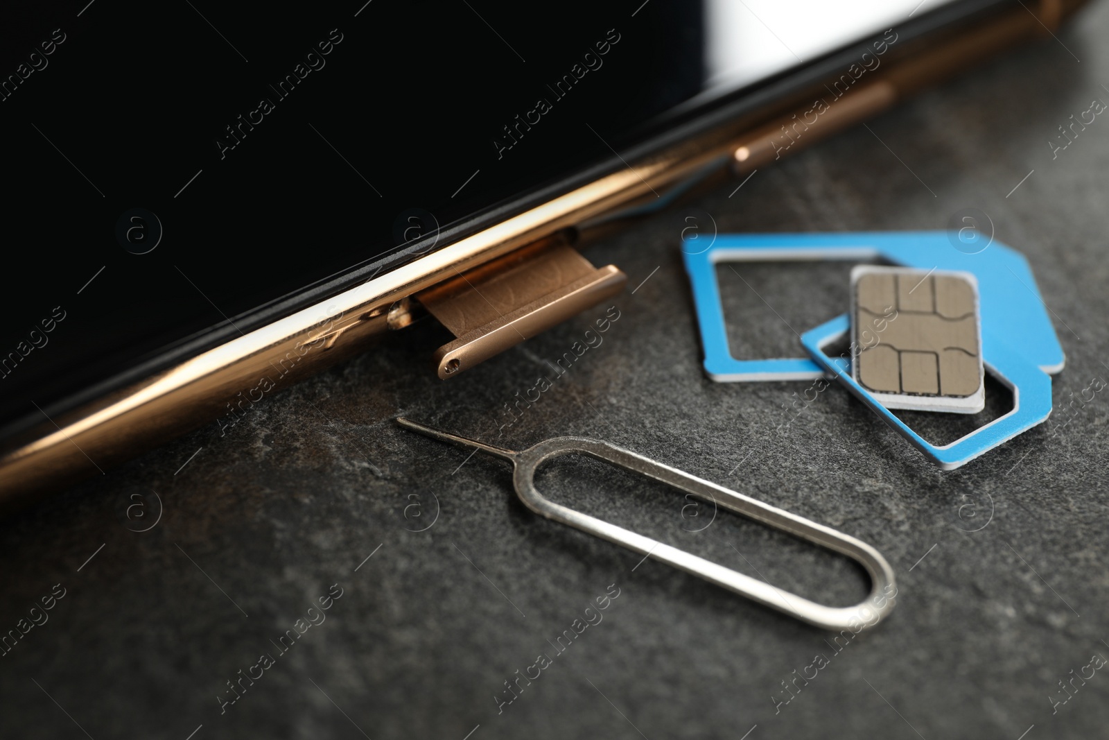 Photo of SIM card, mobile phone and ejector tool on grey table, closeup