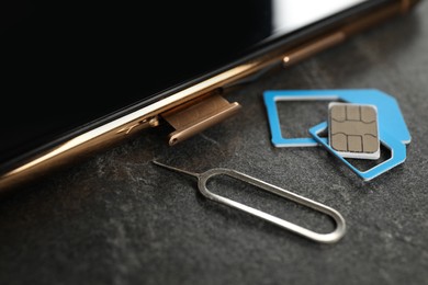 Photo of SIM card, mobile phone and ejector tool on grey table, closeup