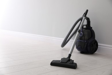 Photo of Modern vacuum cleaner near light wall indoors, space for text