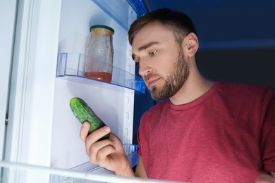 Man taking fresh cucumber out of refrigerator