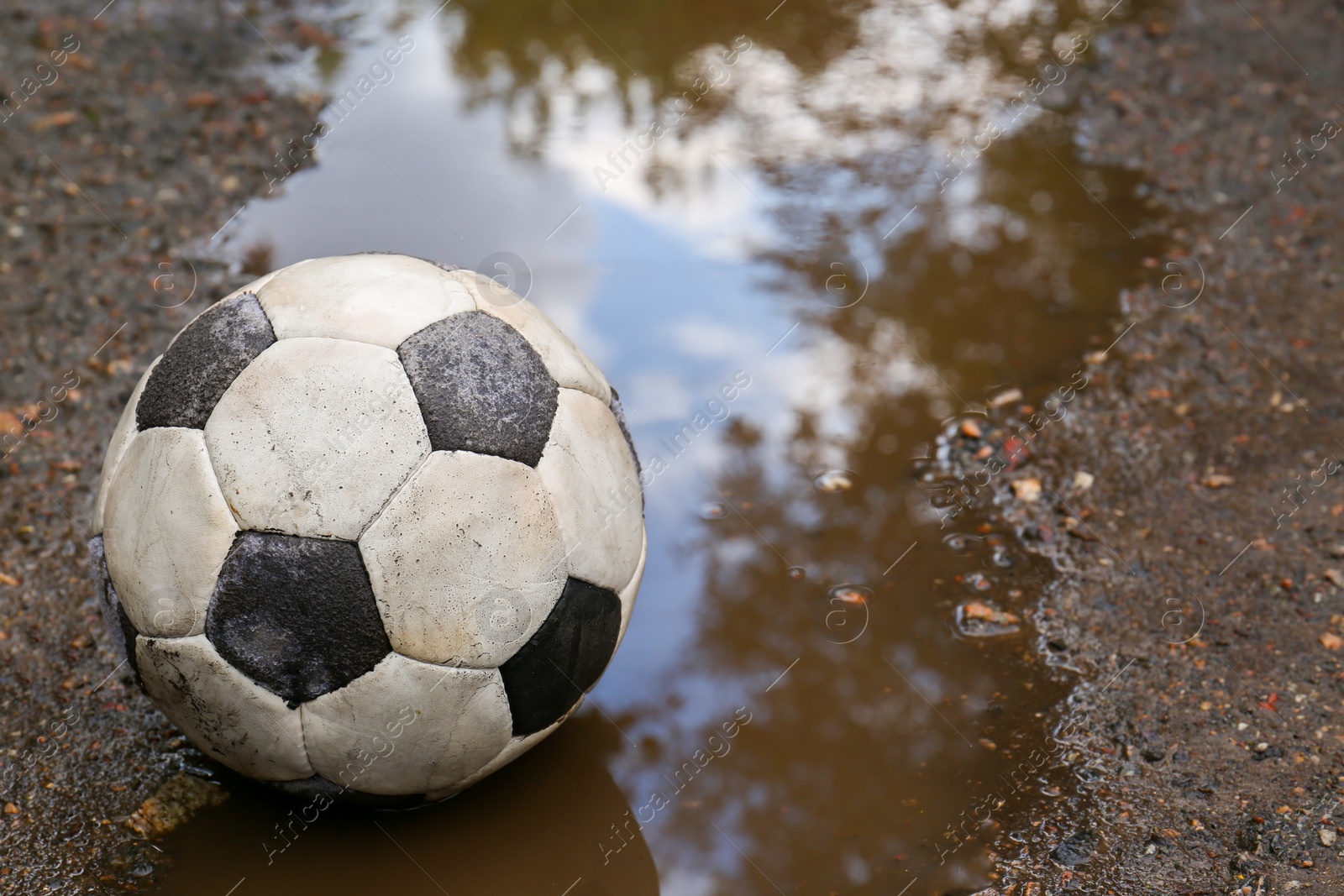 Photo of Dirty soccer ball in muddy puddle, space for text