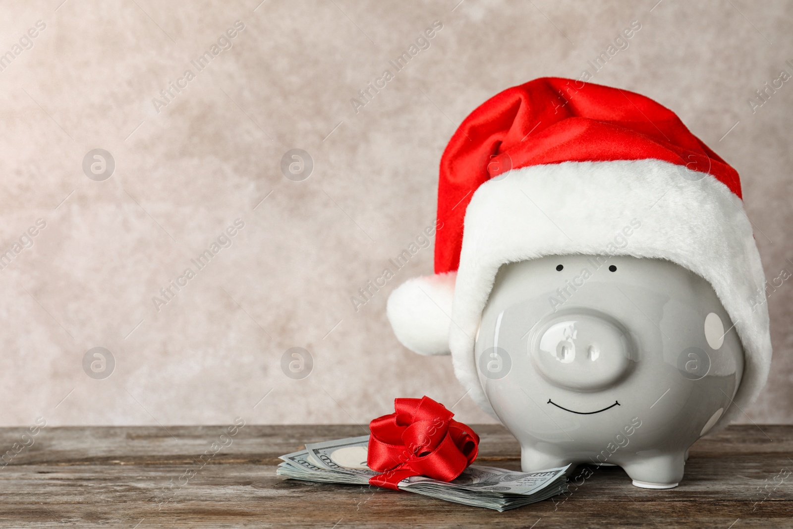 Photo of Piggy bank with Santa hat and dollar banknotes on table. Space for text