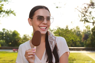 Photo of Beautiful young woman holding ice cream glazed in chocolate outdoors