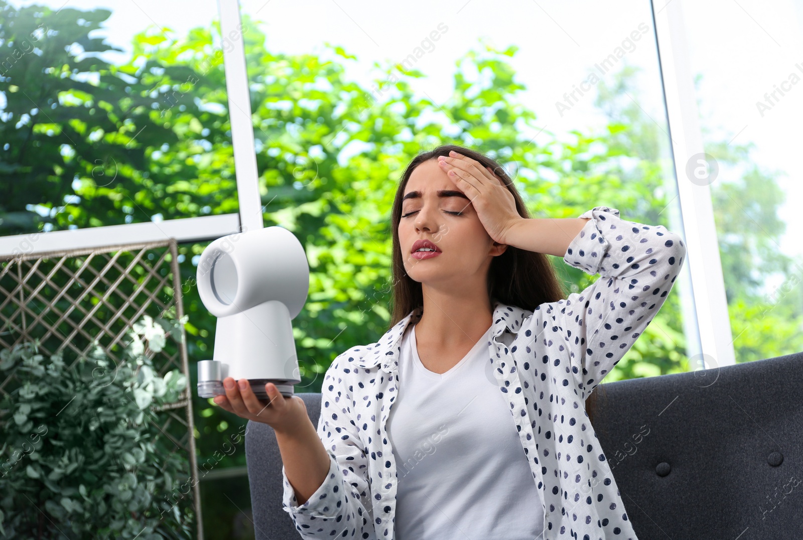 Photo of Woman with portable fan suffering from heat at home. Summer season