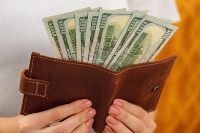 Woman holding brown leather wallet with dollar bills on orange background, closeup. Money exchange