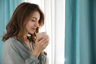 Photo of Woman drinking coffee near window with beautiful curtains at home