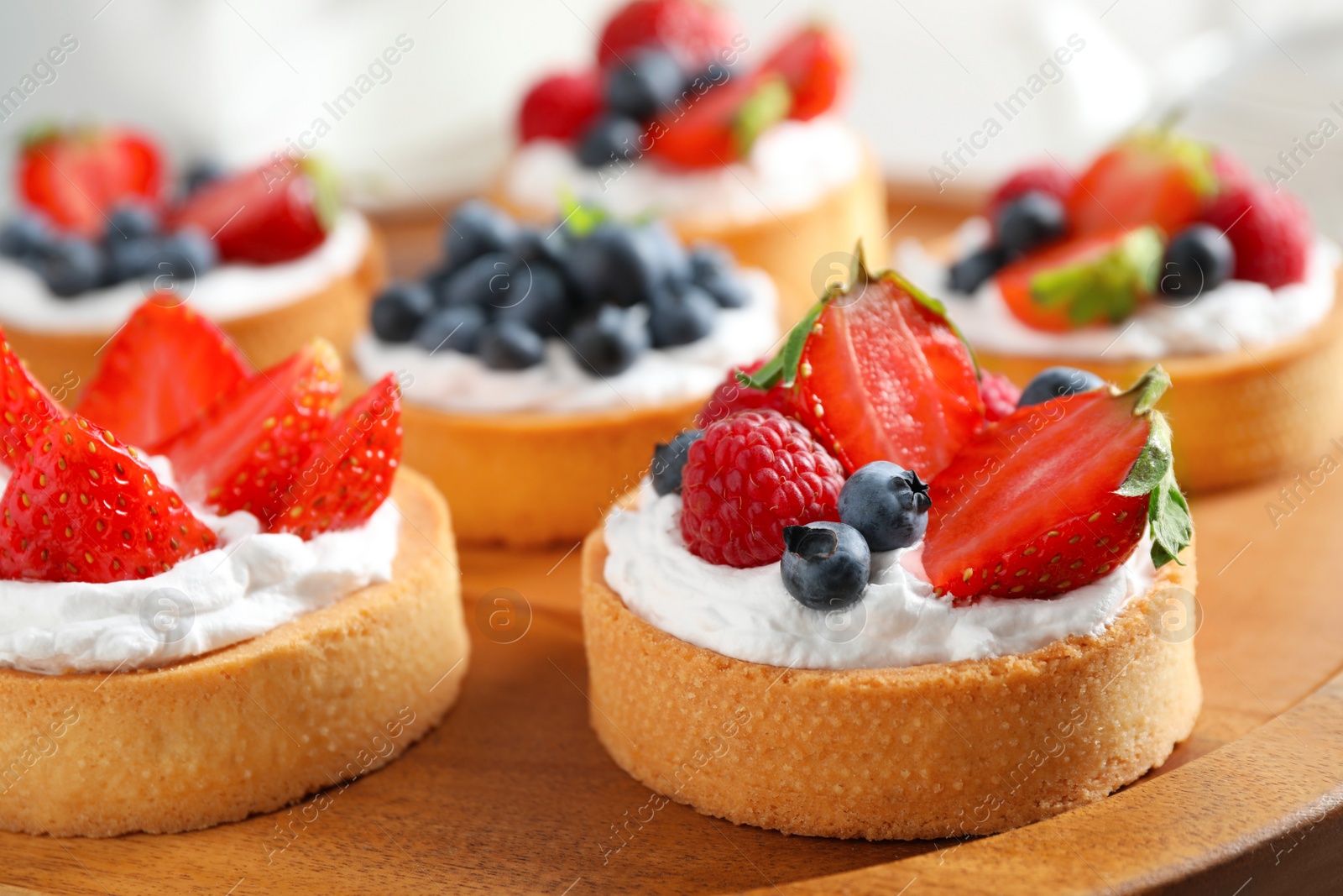 Photo of Wooden plate with different berry tarts. Delicious pastries