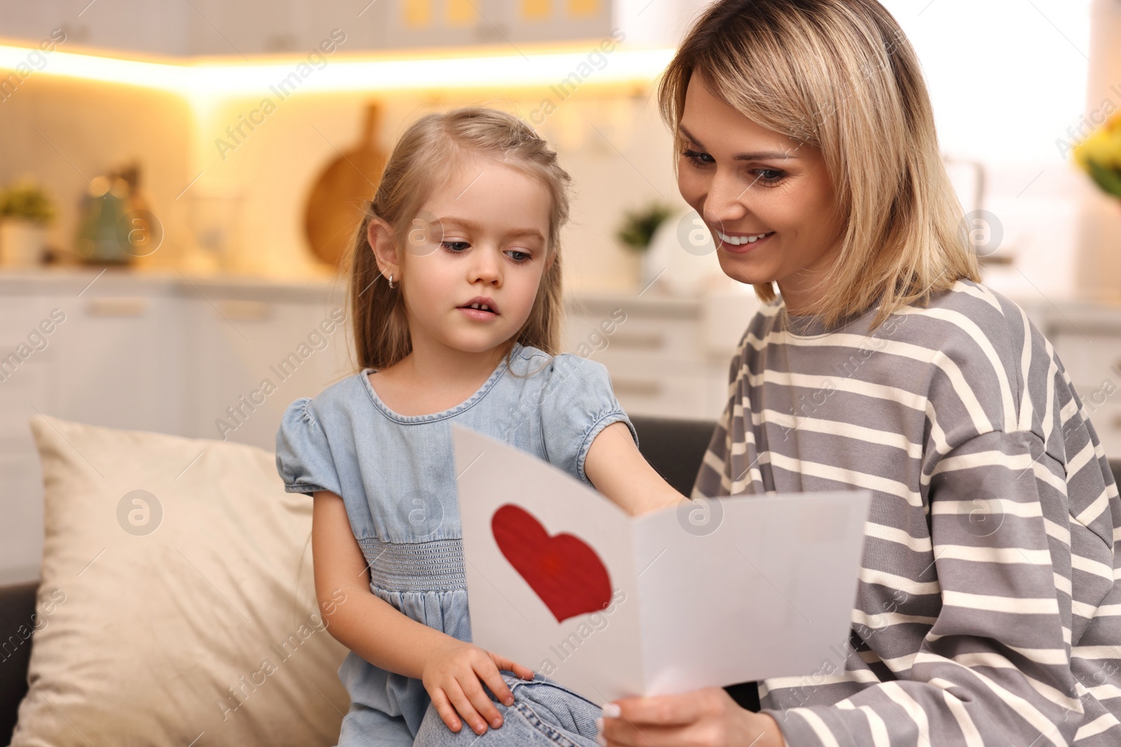 Photo of Little daughter congratulating her mom with greeting card at home. Happy Mother's Day