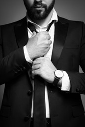 Image of Bearded man tightening tie on grey background, closeup. Black and white effect