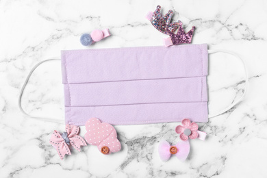 Homemade protective mask and adorable girly hair clips on white marble background, flat lay. Sewing for child