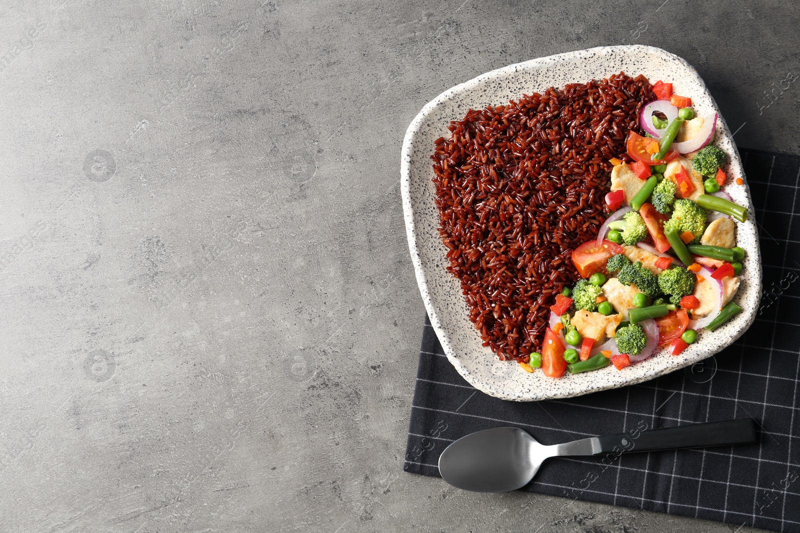 Photo of Plate with cooked brown rice and spoon on table, top view. Space for text