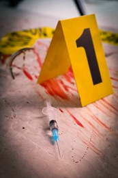 Photo of Syringe in blood and crime scene marker on marble table, closeup