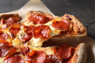 Taking piece of tasty pepperoni pizza at grey table, closeup