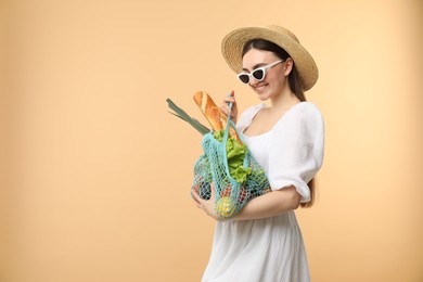 Photo of Woman with string bag of fresh vegetables and baguette on beige background, space for text