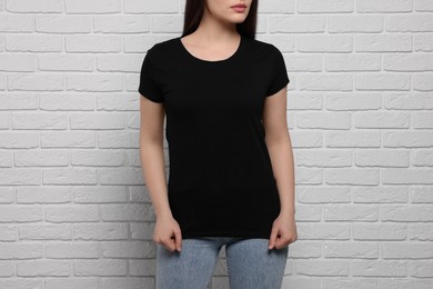 Woman wearing stylish black T-shirt near white brick wall, closeup