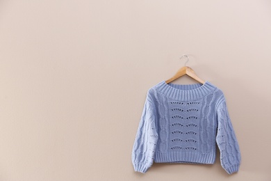 Hanger with stylish sweater on beige wall. Space for text