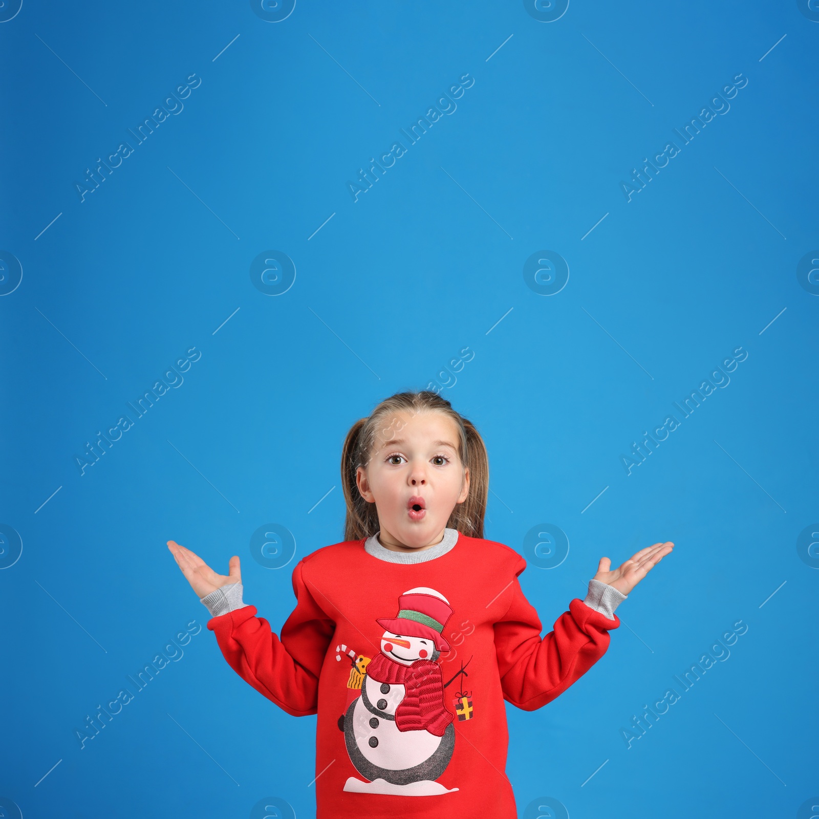 Photo of Surprised little girl in Christmas sweater on blue background, space for text