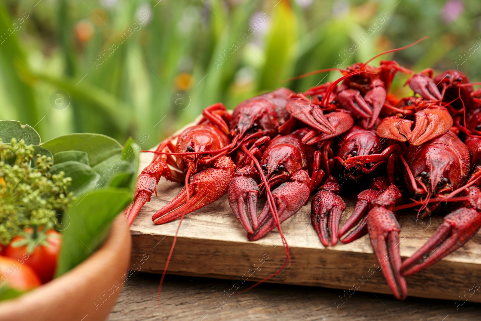 Photo of Delicious red boiled crayfish and products in bowl on wooden table