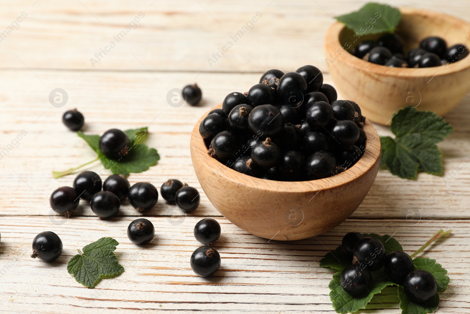 Photo of Ripe blackcurrants and leaves on light wooden table, closeup