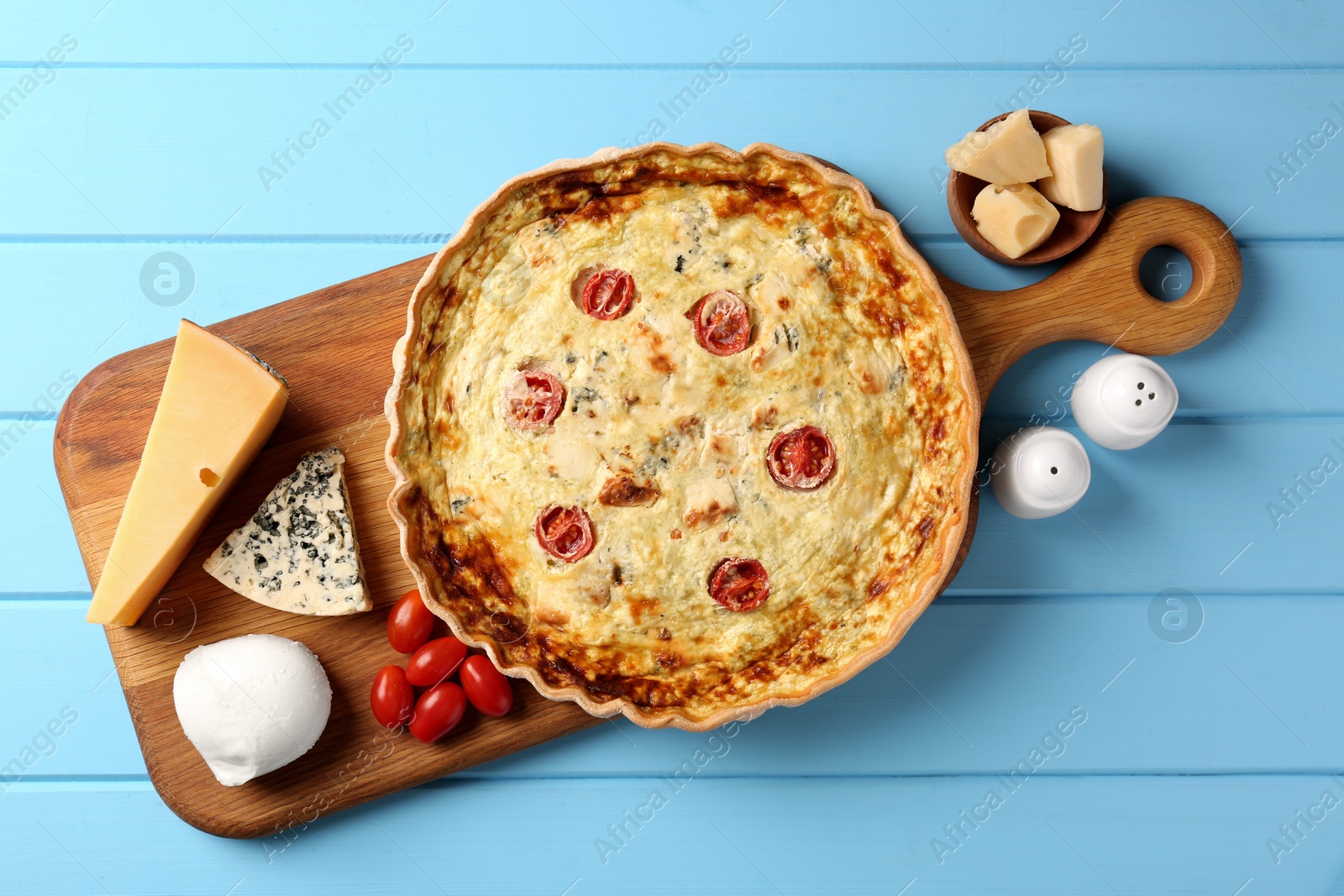 Photo of Delicious homemade cheese quiche and ingredients on light blue wooden table, flat lay