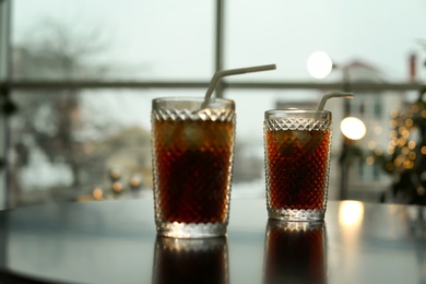 Photo of Glasses of cold cola on table against blurred background