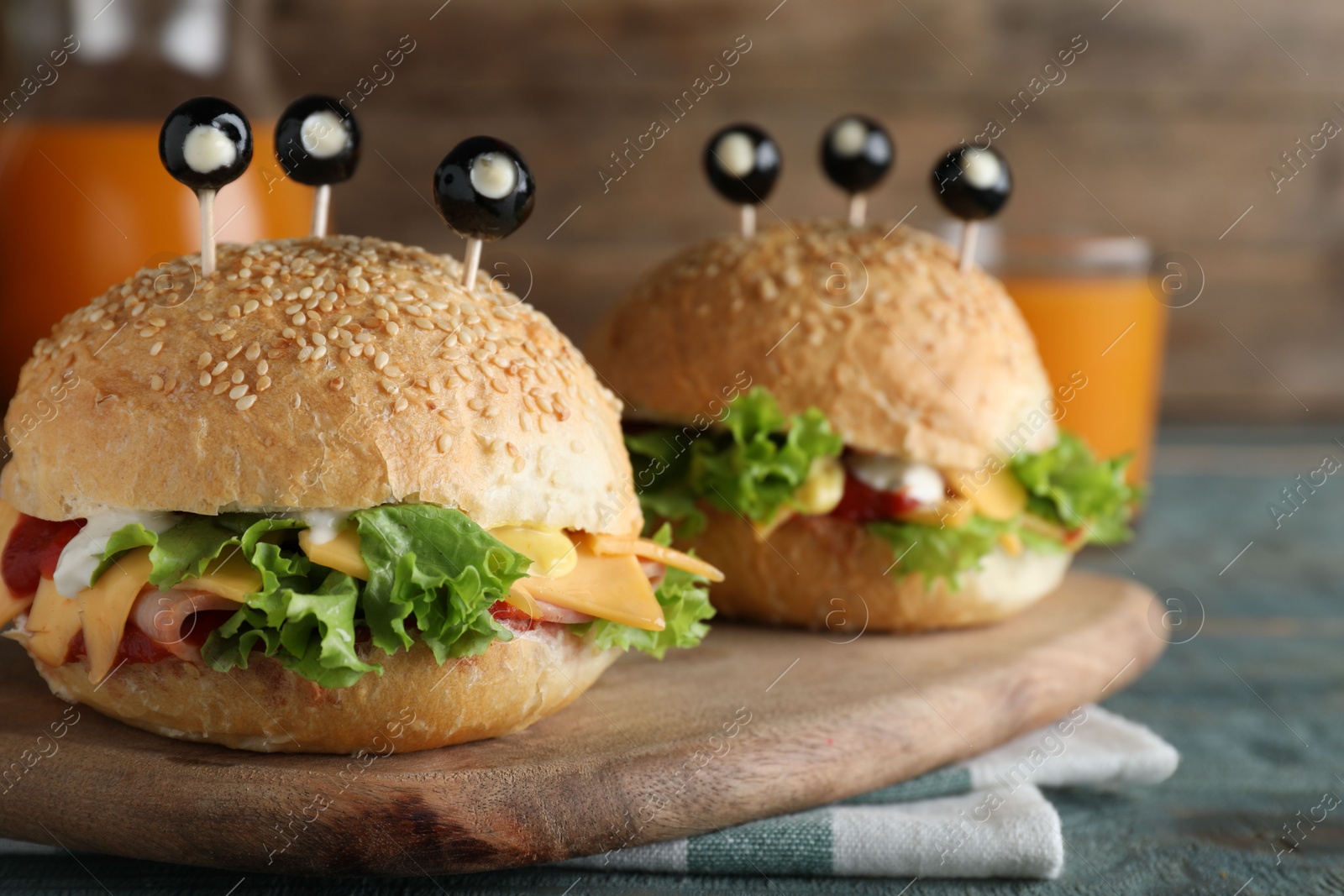 Photo of Cute monster burgers served on blue wooden table. Halloween party food