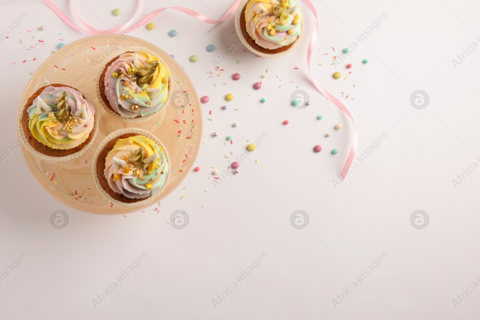 Photo of Dessert stand with cute sweet unicorn cupcakes on white table, flat lay. Space for text