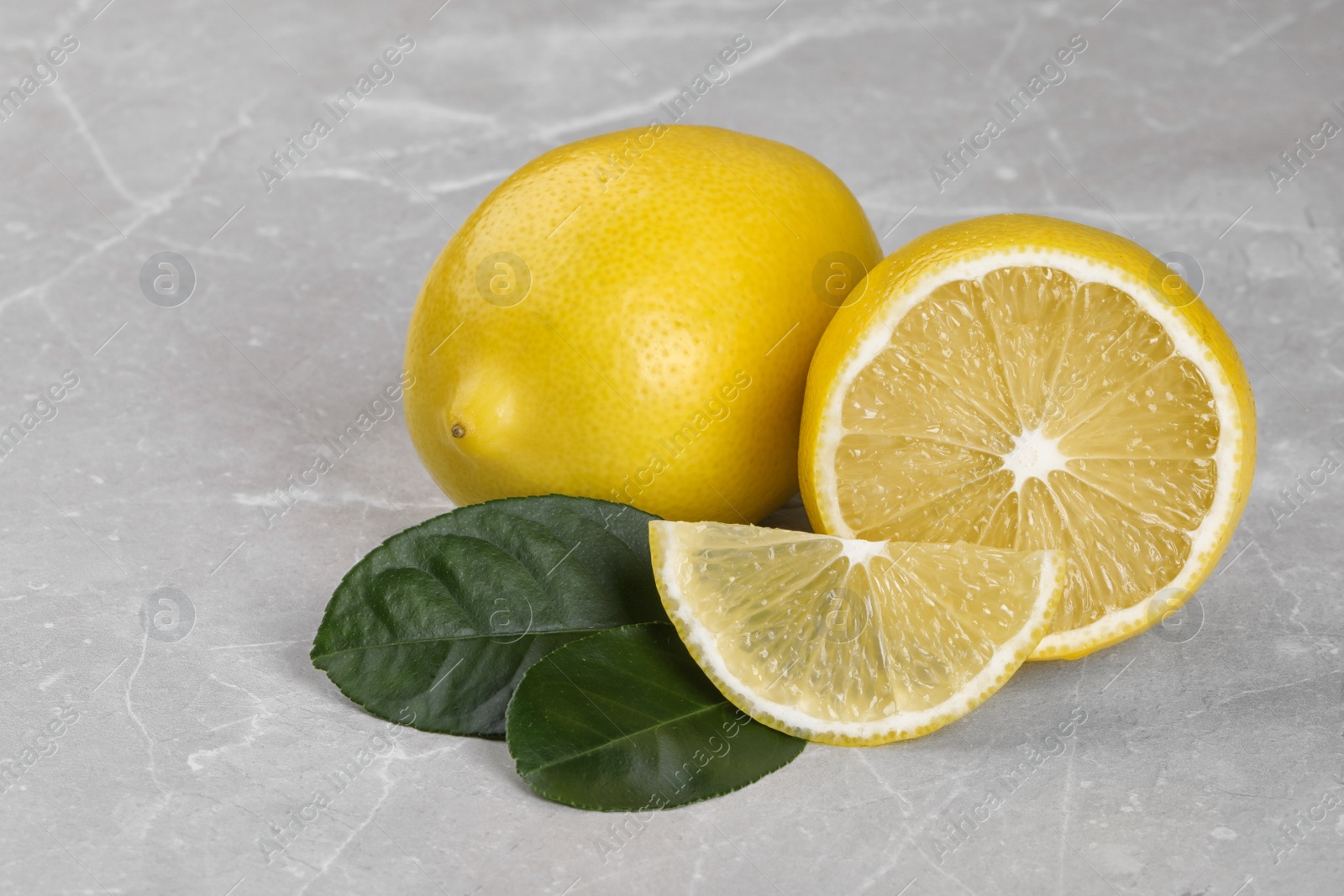 Photo of Whole and cut fresh lemon and green leaves on grey table