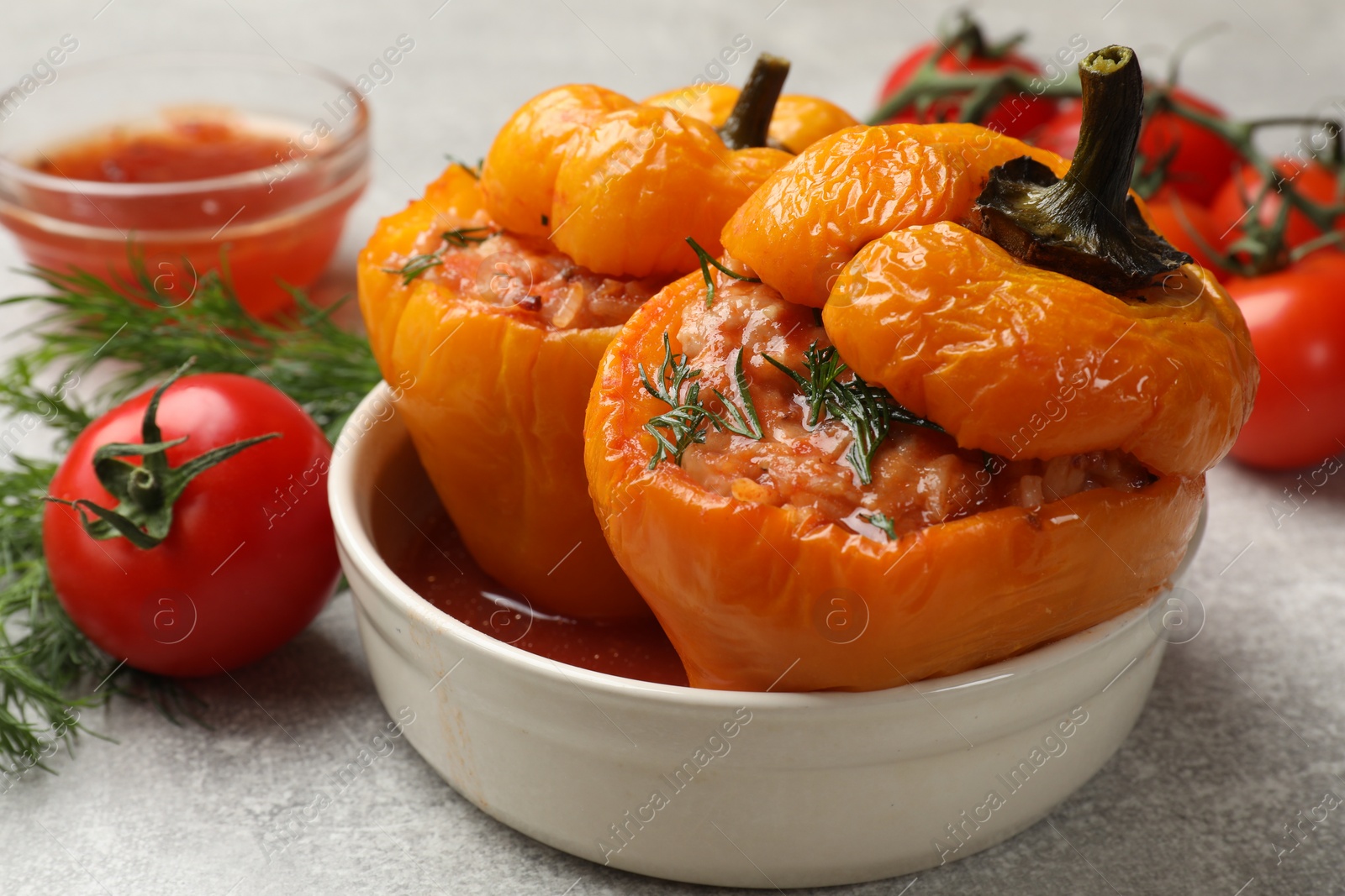 Photo of Tasty stuffed peppers in bowl, dill and tomato on light grey table, closeup