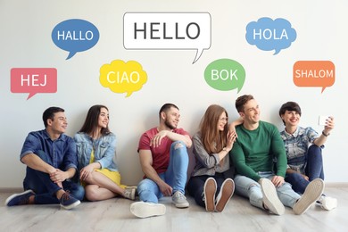Happy people sitting near light wall and illustration of speech bubbles with word Hello written in different languages