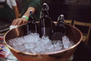 Bottles of beer served in metal bowl with ice on table