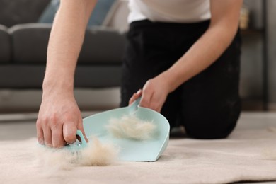 Photo of Man with brush and pan removing pet hair from carpet at home, closeup