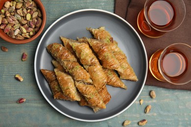Photo of Delicious baklava with pistachios, scattered nuts and hot tea on light blue wooden table, flat lay