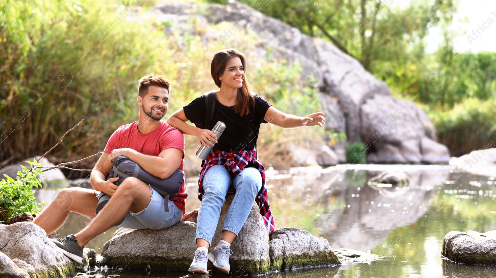 Photo of Young happy couple sitting on rock outdoors. Camping vacation