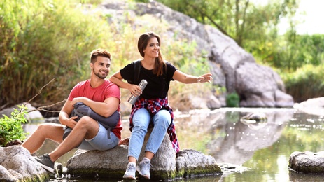 Photo of Young happy couple sitting on rock outdoors. Camping vacation