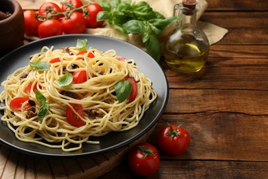 Photo of Delicious pasta with anchovies, tomatoes and basil on wooden table. Space for text