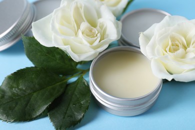 Different lip balms and rose flowers on light blue background, closeup