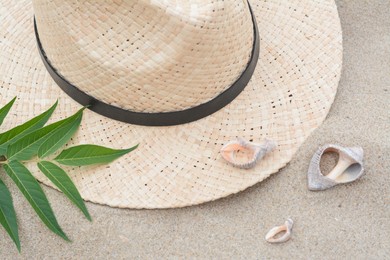 Straw hat, seashells and green leaves on sandy beach, flat lay