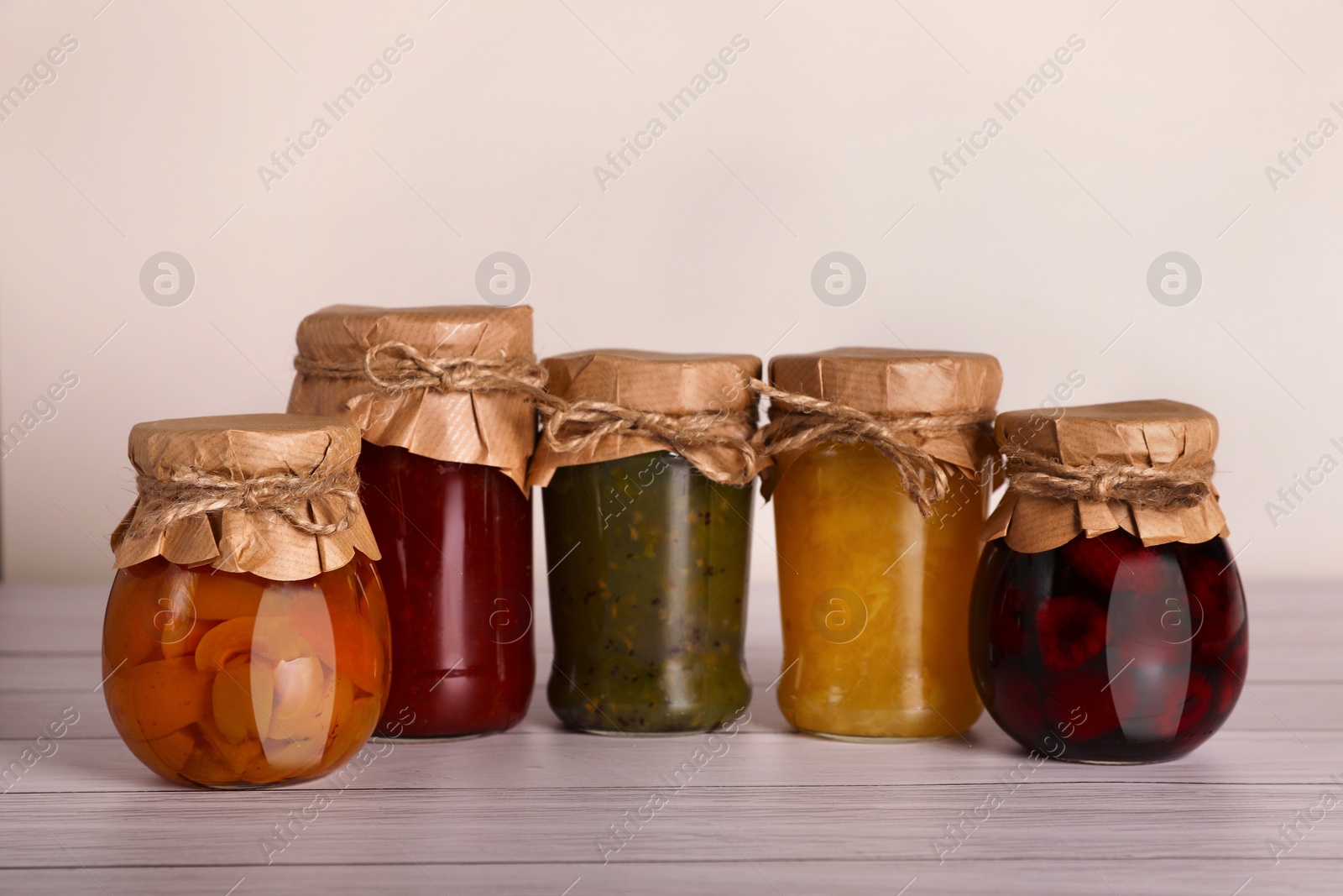 Photo of Jars with preserved fruit jams on white wooden table