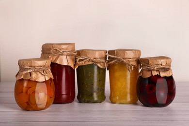Jars with preserved fruit jams on white wooden table