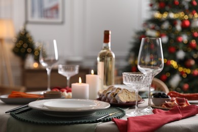 Photo of Christmas table setting with burning candles, appetizers and dishware indoors